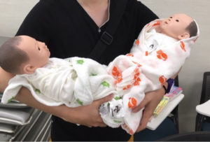 杏林大学医学部附属病院のあんずくらぶにて双子に模した人形を抱っこする夫